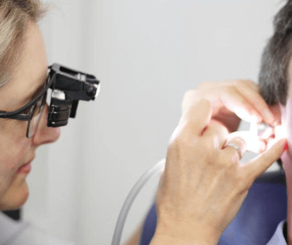 A clinician wearing magnifying loupes with a light works in a patient's ear with a suction tube